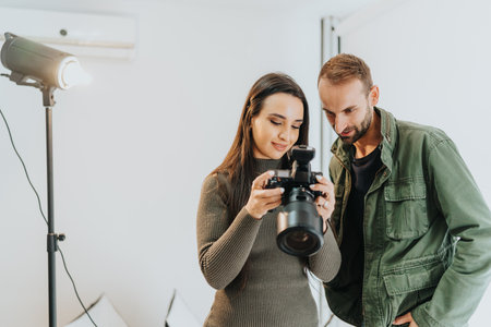 Two individuals collaborating while reviewing camera photos in a well-lit studio space.