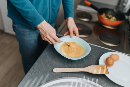 Man preparing scrambled eggs in the kitchen for breakfast.
