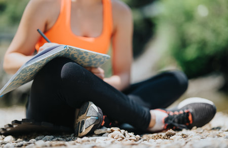 Woman writing in a notebook while sitting outdoors on a sunny dayの写真素材