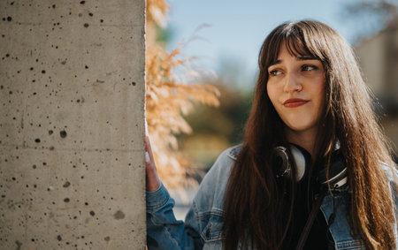 Young woman with headphones leaning on wall in outdoor autumn setting