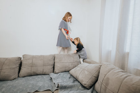 Two young girls playing together on a sofa in a cozy living roomの写真素材