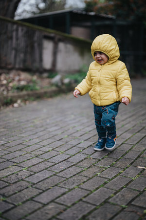 Young child in yellow jacket walking outdoors on a chilly dayの写真素材