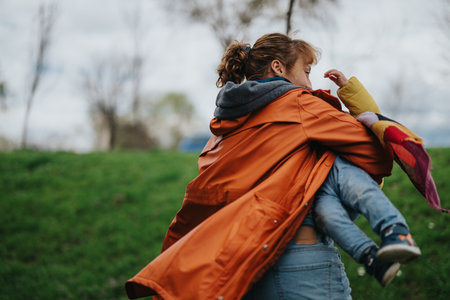 Mother carrying her child outdoors on a breezy day in the parkの写真素材