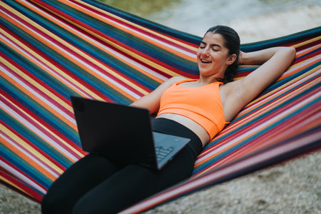 Woman relaxing on colorful hammock while working on laptop outdoorsの写真素材