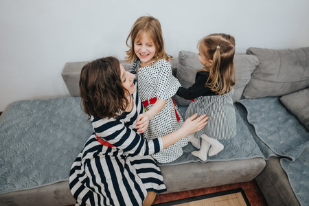 Mother sharing a joyful moment with her two daughters on the couchの写真素材