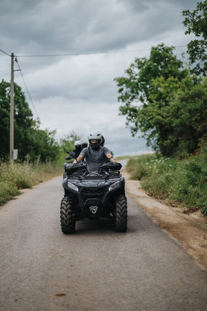 Riders on Quad Bike Exploring Scenic Countryside Road with Clouds Above