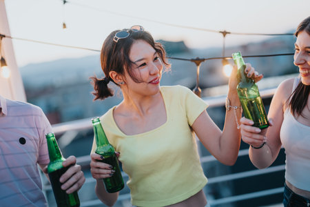 Friends enjoying a cheerful rooftop party with beverages during sunsetの写真素材