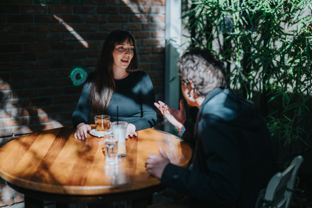 Two individuals having a conversation at a sunlit outdoor table.の写真素材