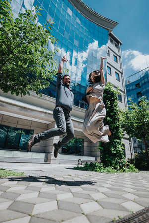 Excited business colleagues jumping outdoors near a modern corporate buildingの写真素材