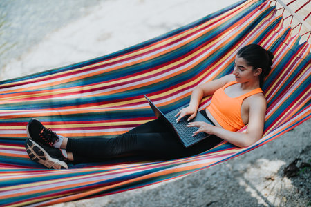 Young woman works remotely on laptop while lying in a colorful hammockの写真素材