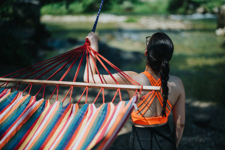 Woman relaxing by a river on a colorful striped hammock outdoors