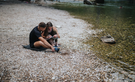 Couple Enjoys Reading and Relaxation Along a Pebbled Riverside Beach