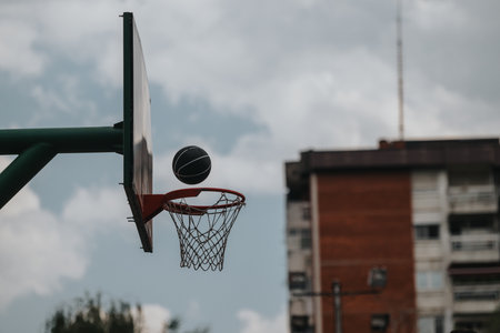 Basketball in action at an outdoor court near urban buildings under cloudy sky