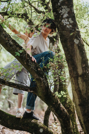 Two women explore a mossy forest, climbing a tree branch and enjoying nature togetherの写真素材