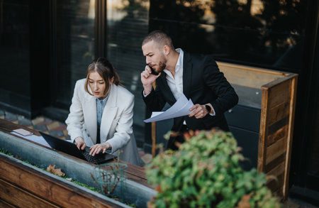 Two professionals collaborate outdoors while focused on work and problem solving