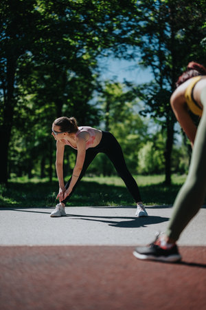 Two women stretching outdoors in a park during a fitness session