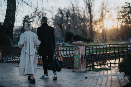 Two people walking together in a park during a gentle golden sunsetの写真素材