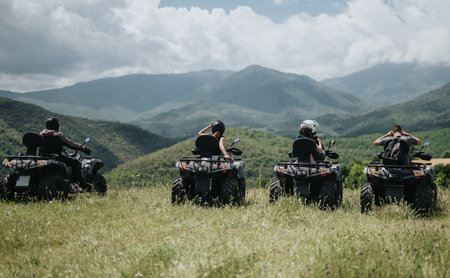 Group of friends riding quad bikes through scenic green hills below cloudy skiesの写真素材