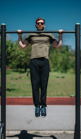 Man performing pull-ups on outdoor exercise bar in a scenic park setting