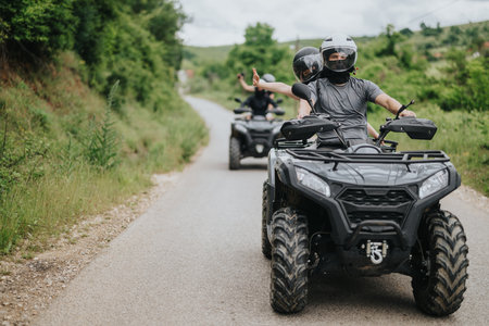 Friends riding quad bikes on a rural road in a scenic green areaの写真素材