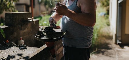 Man in gray tank top repairs a garden trimmer with wires outdoorsの写真素材
