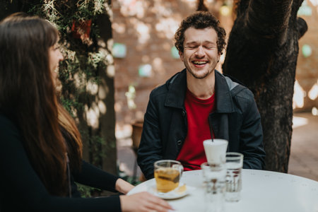 Young couple enjoying laughter while sitting together at an outdoor cafeの写真素材