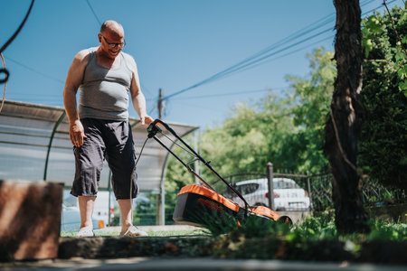 Older man mowing the lawn in a sunny backyard with a lawn mowerの写真素材