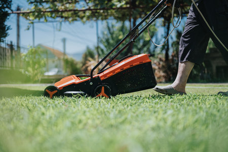 Person mowing lawn with orange and black lawn mower in a sunny backyard for outdoor yard work