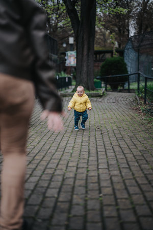 Child walking outside wearing a yellow jacket with arms extended reaching forward