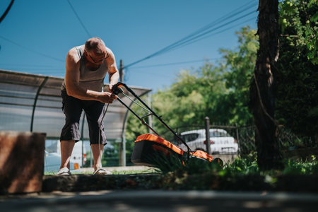 Man mowing the yard with a lawn mower outdoors on a sunny day in the backyard