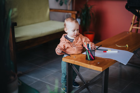 Young child playing with colorful markers on a wooden table indoorsの写真素材