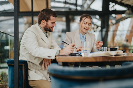 Two professionals collaborating over a document at a bright modern cafeの写真素材