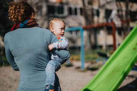 Mother carrying her child at an outdoor playground on a sunny dayの写真素材