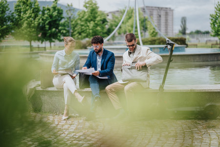 Business colleagues discussing documents while seated outdoors with scooter nearbyの写真素材