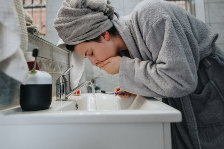 Woman in bathroom washing face while wearing a bathrobe and towel turban