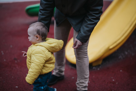 Child in yellow jacket plays near a slide in a playgroundの写真素材