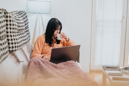 Woman relaxing at home with a laptop and hot beverage on a couchの写真素材