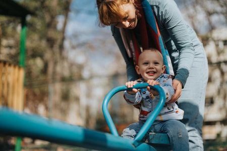Mother guiding her happy child on a seesaw in the parkの写真素材