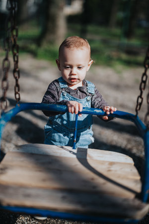 Young child playing with a wooden swing outdoors on a sunny dayの写真素材