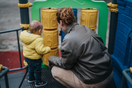 Parent and child playing together on a colorful playground equipment outdoorsの写真素材
