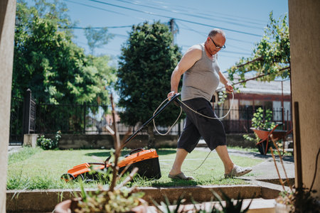 Older man mowing the lawn in a sunny backyard with a corded lawn mowerの写真素材
