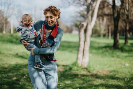 Joyful mother carrying her child in a sunny park settingの写真素材