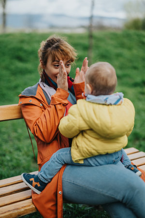 Mother playing with her child on a bench in a green parkの写真素材