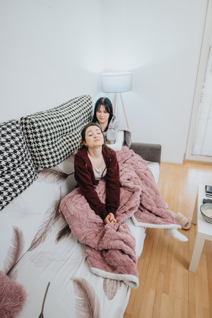 Friends relaxing together on a cozy couch with warm blankets at homeの写真素材