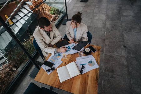 Two professionals discussing data charts during a business meeting in a modern officeの写真素材