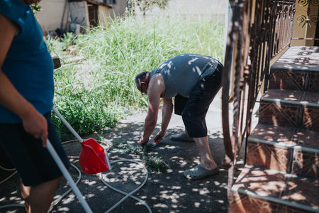 People gardening outdoors in a sunny yard; kneeling to weed and tend plants near stairs.の写真素材