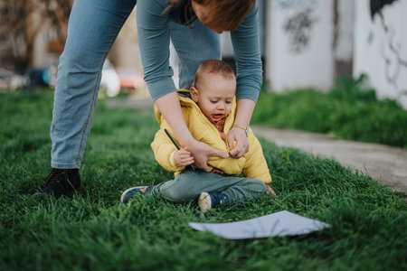 Mother helping her young child outdoors in a green grassy parkの写真素材