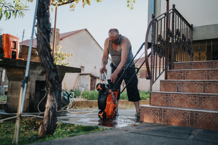 Man using pressure washer to clean driveway outside home near stairs at duskの写真素材