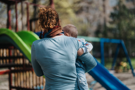 Mother carrying her child at an outdoor playground on a sunny dayの写真素材