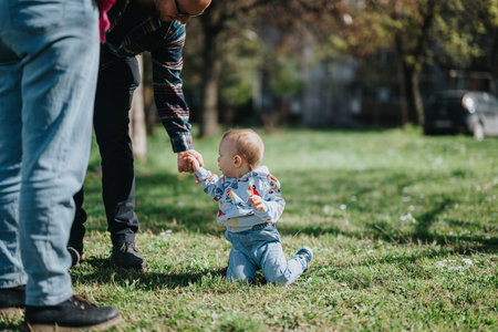 Parent assisting a toddler learning to walk outdoors in a sunny parkの写真素材